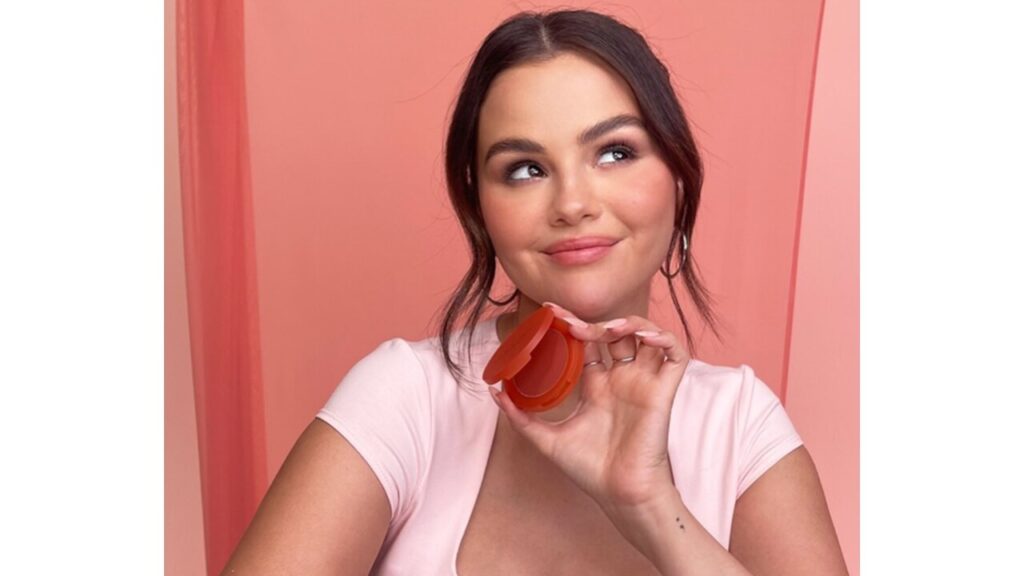 Selena Gomez holding a Rare Beauty product.
